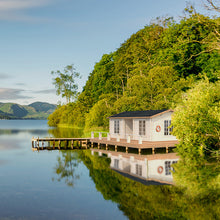 Load image into Gallery viewer, A serene lakeside setting featuring the Cabin New Zealand 343 Sq.ft. The cabin is positioned on a wooden deck with a view of the water, surrounded by lush greenery, creating the perfect retreat by WholeWoodCabins