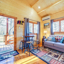 Load image into Gallery viewer, Wooden cabin interior with a living area, dining table, and decor.