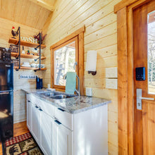 Load image into Gallery viewer, Small kitchen with wooden walls and a sink area.