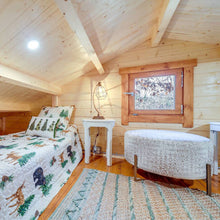 Load image into Gallery viewer, Wooden cabin loft bedroom with two beds, a lamp, and a window.