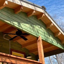 Load image into Gallery viewer, Close-up of cabin roof with exposed wooden beams and green siding, highlighting natural wood construction and ceiling fan on the porch by WholeWoodCabins

