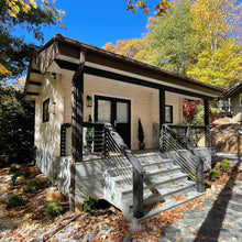 Load image into Gallery viewer, Cabin with a wooden porch and steps, surrounded by trees with autumn foliage.

