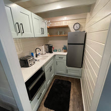 Load image into Gallery viewer, Small cabin kitchen with white cabinets, black appliances, and a clock on the wall.
