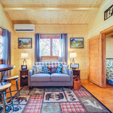 Load image into Gallery viewer, Living room in a wooden cabin with a sofa, rug, and decor
