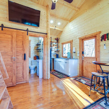 Load image into Gallery viewer, Wooden interior of a cabin with a kitchen area, bathroom, and living space.
